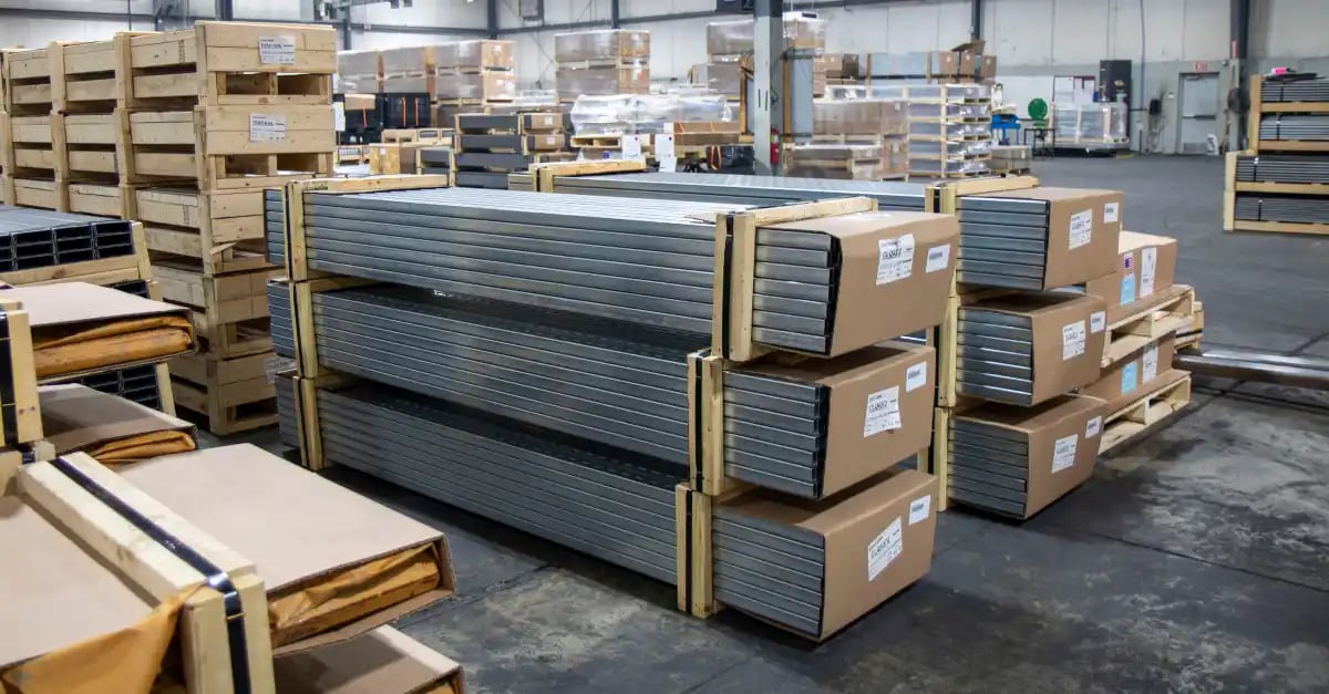 Palletized and cardboard-capped bundles of steel framing channels stacked on a warehouse floor.